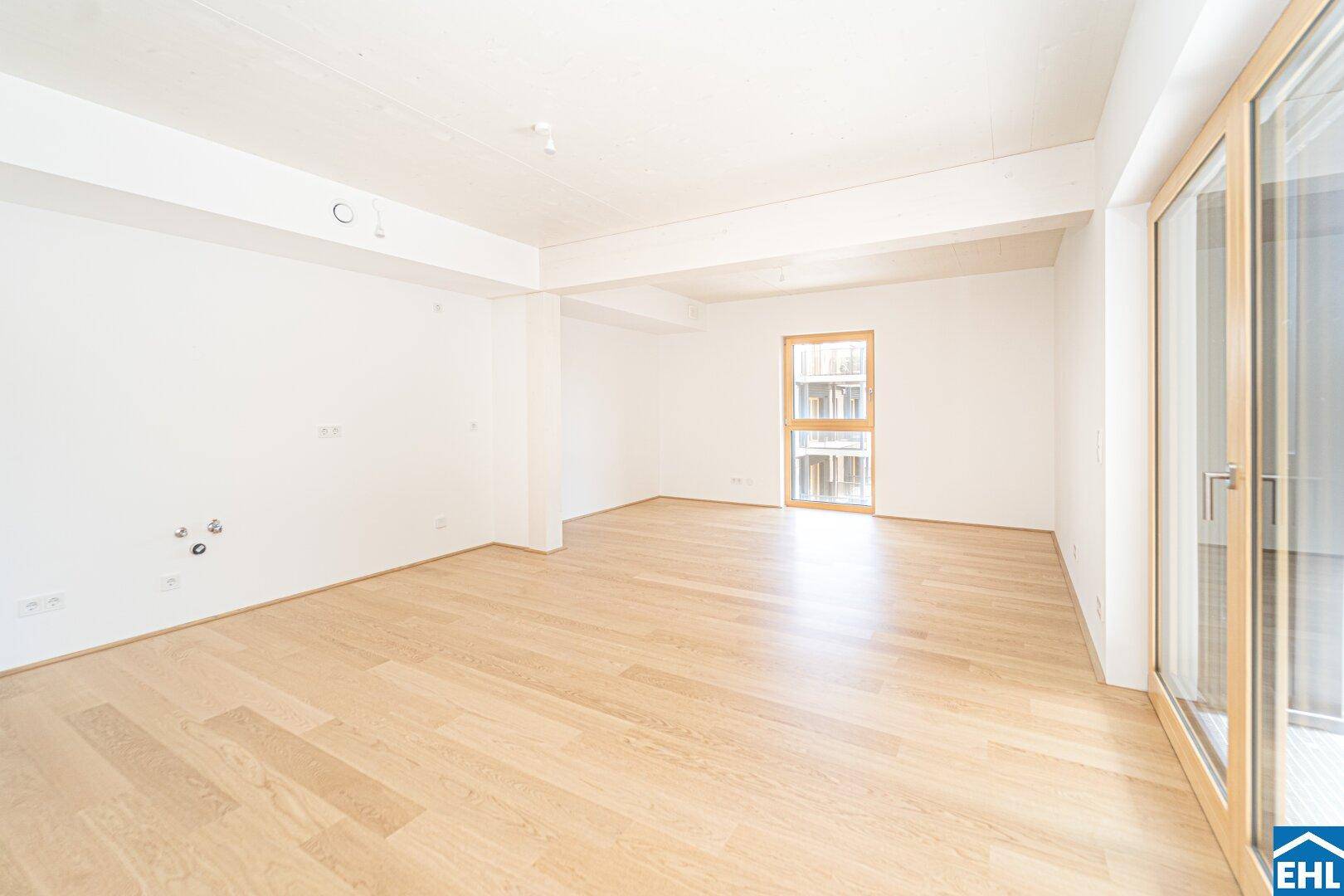 Geräumiger Wohnbereich mit Holzboden und Zugang zu einem Balkon oder einer Terrasse.