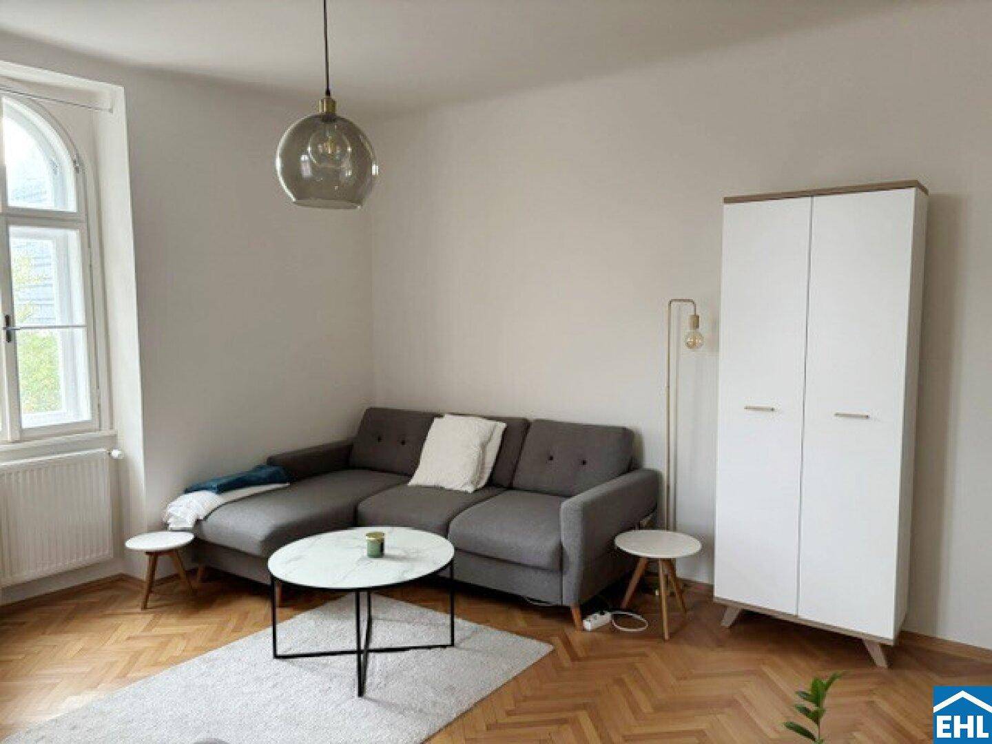Gemütliches Wohnzimmer mit grauem Sofa, Beistelltischen und einem modernen Kleiderschrank.