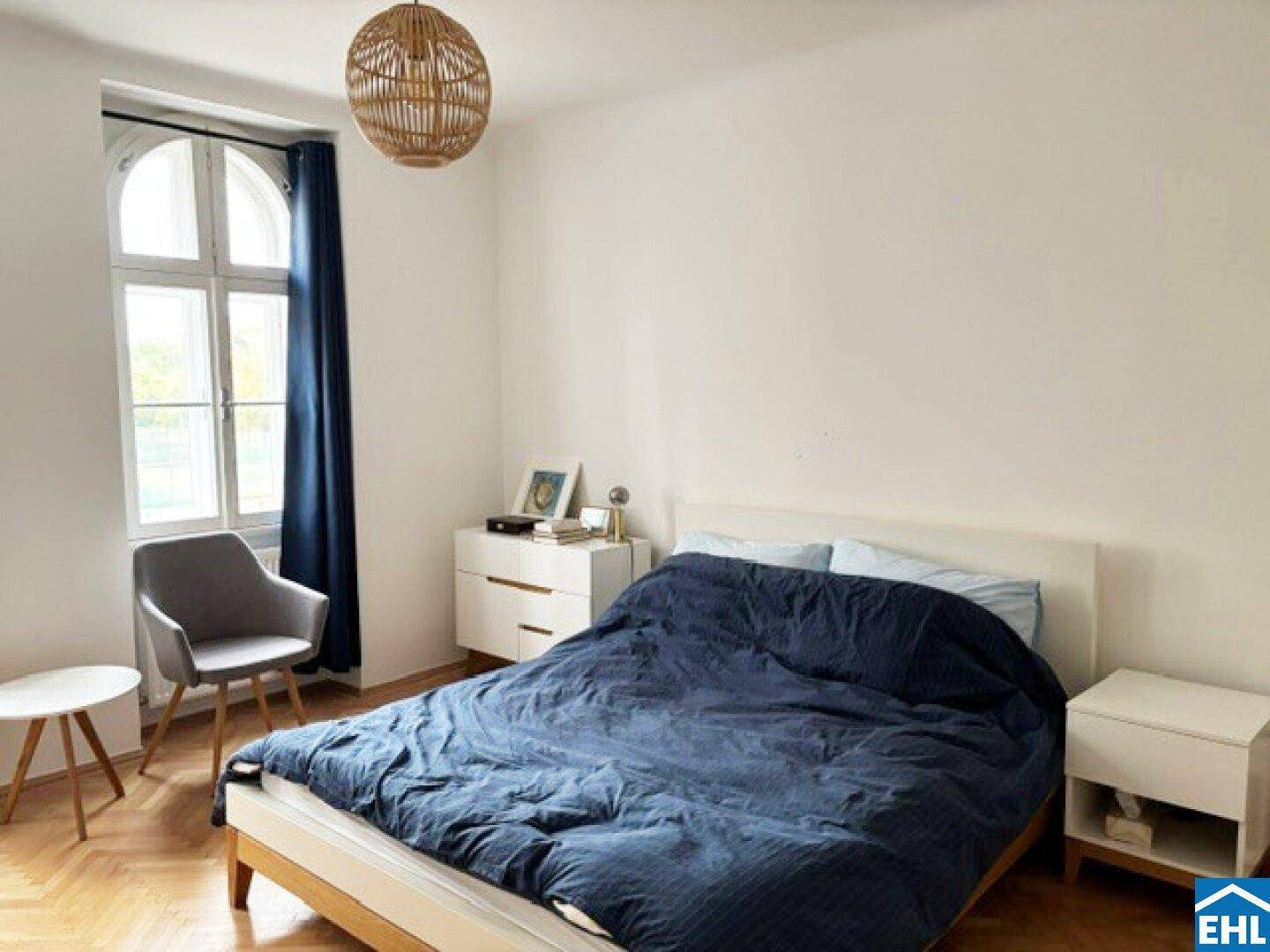 Schlafzimmer mit Doppelbett, Nachttischen und einem großen Fenster mit blauen Vorhängen.