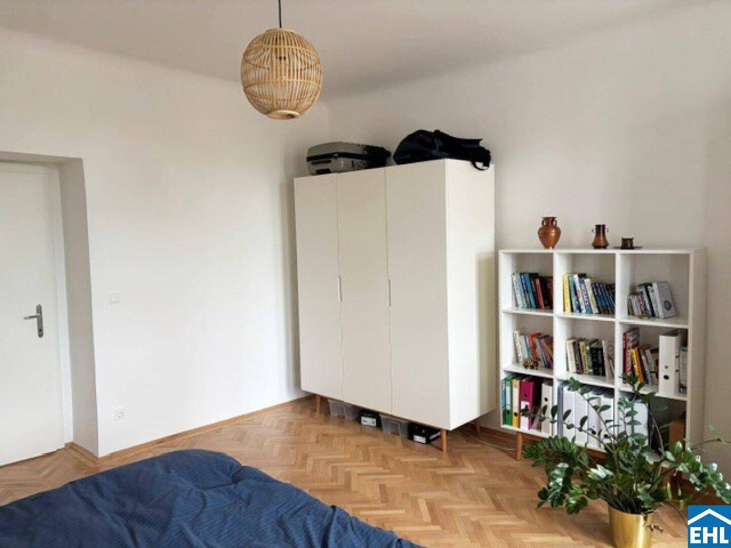 Schlafzimmer mit weißem Kleiderschrank, Bücherregal und Pflanzen, schafft eine wohnliche Umgebung.