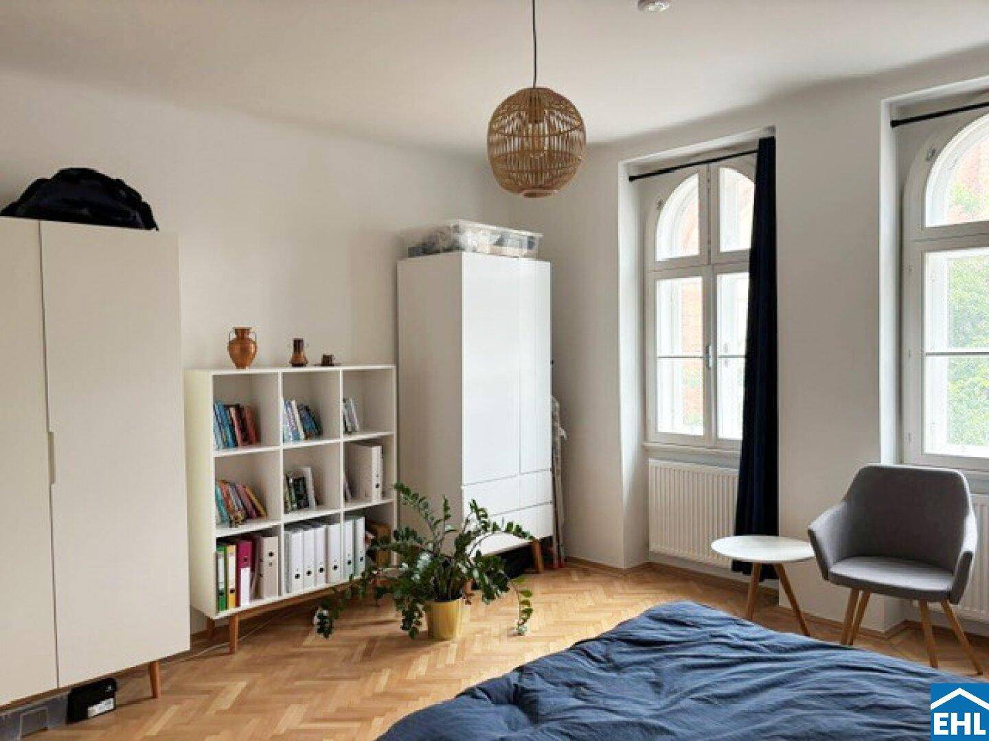 Helles Schlafzimmer mit zwei Fenstern, Holzboden und einem gemütlichen Sessel.