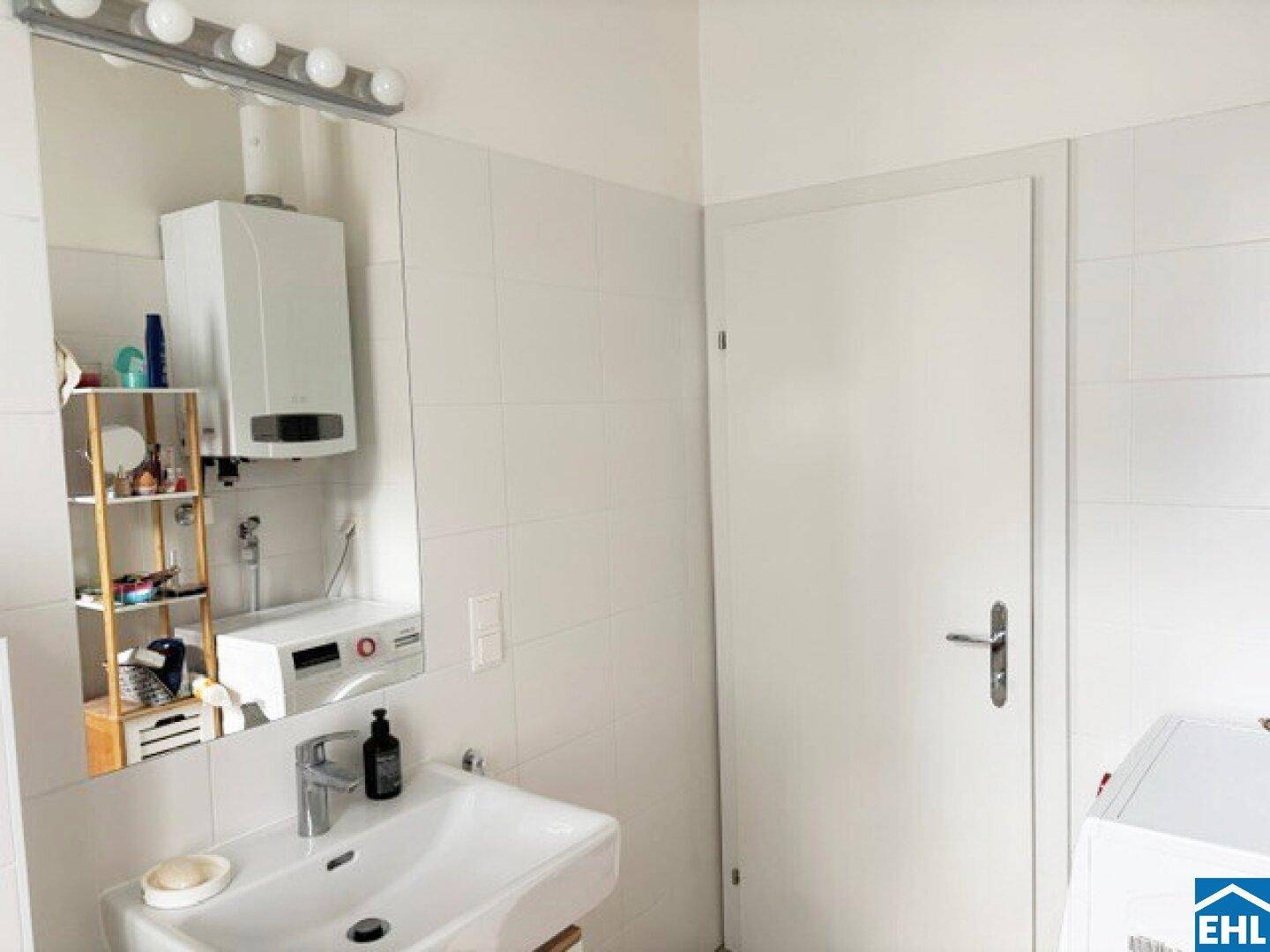 Helles Badezimmer mit Waschbecken, großem Spiegel, Spiegelschrank und Waschmaschine.