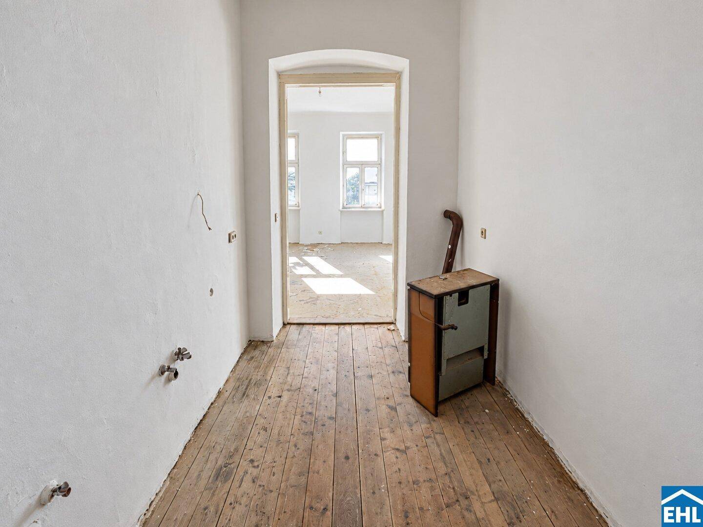 Flur mit freigelegten Holzdielen und einem Durchgang zu einem weiteren hellen Raum.