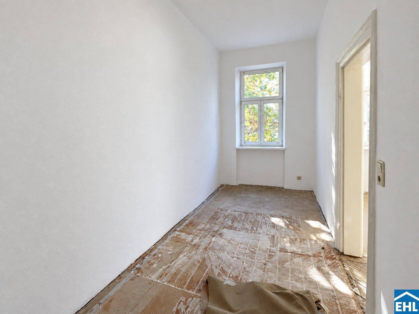 Schmaler, heller Raum mit Holzdielenboden und einem Fenster, ideal für ein kleines Zimmer.