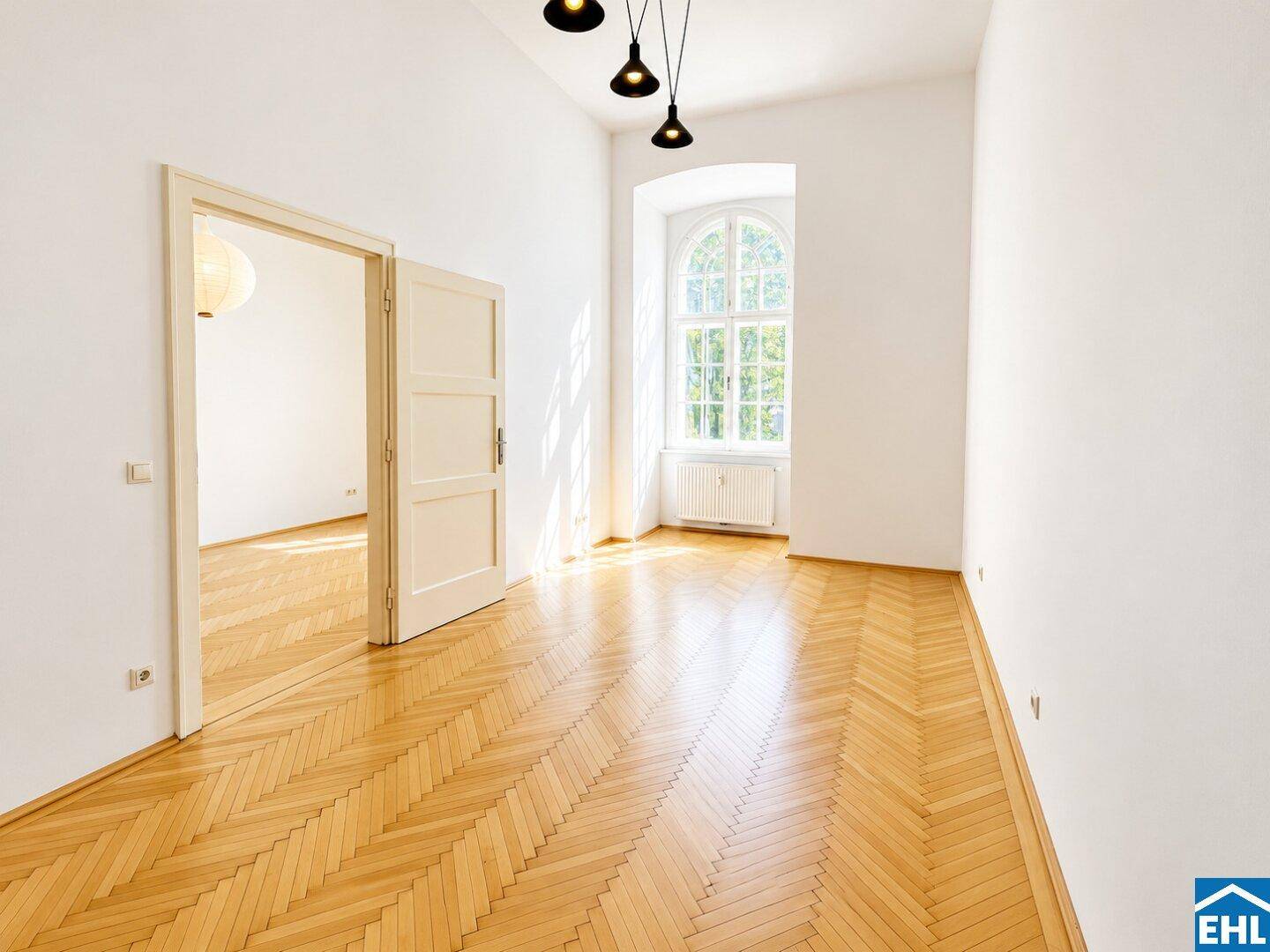 Geräumiger Wohnbereich mit elegantem Fischgrätparkett, hohen Decken und modernen Pendelleuchten.