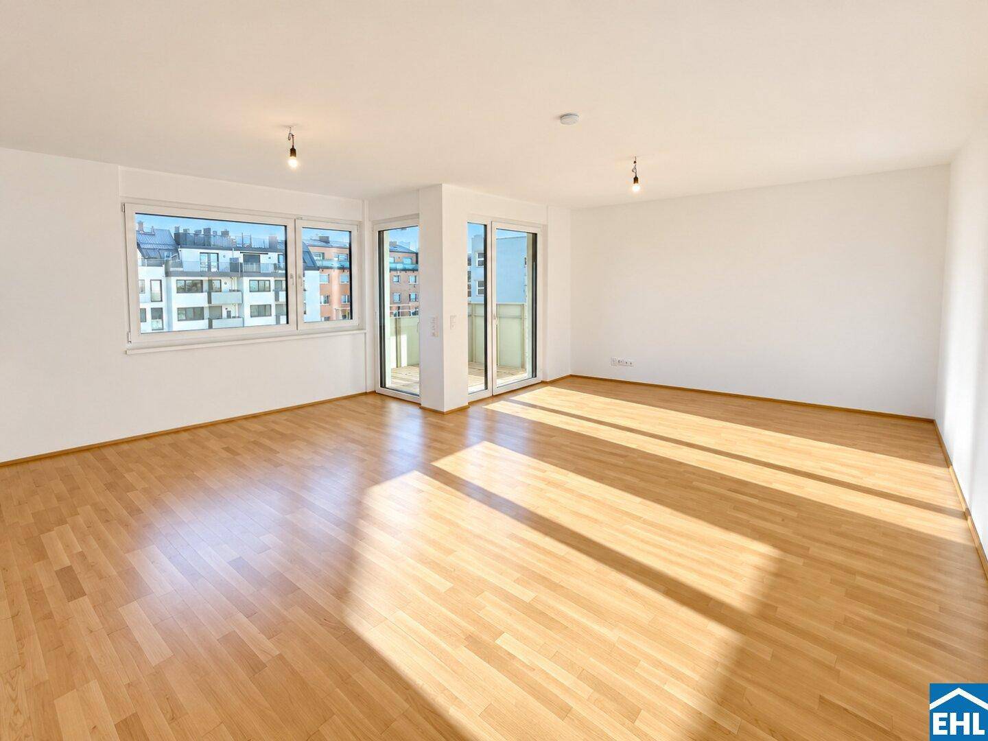 Geräumiges, lichtdurchflutetes Wohnzimmer mit Holzboden und direktem Zugang zum Balkon.