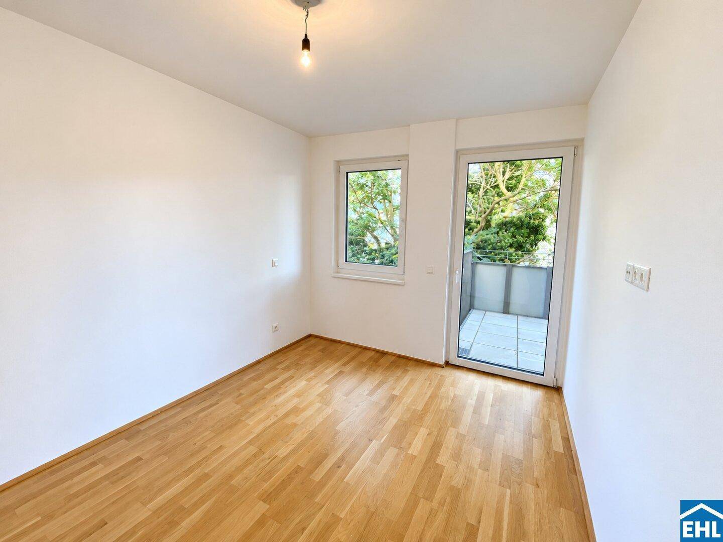 Helles Schlafzimmer mit Holzboden, Fenster und Zugang zu einem Außenbereich mit grüner Aussicht.