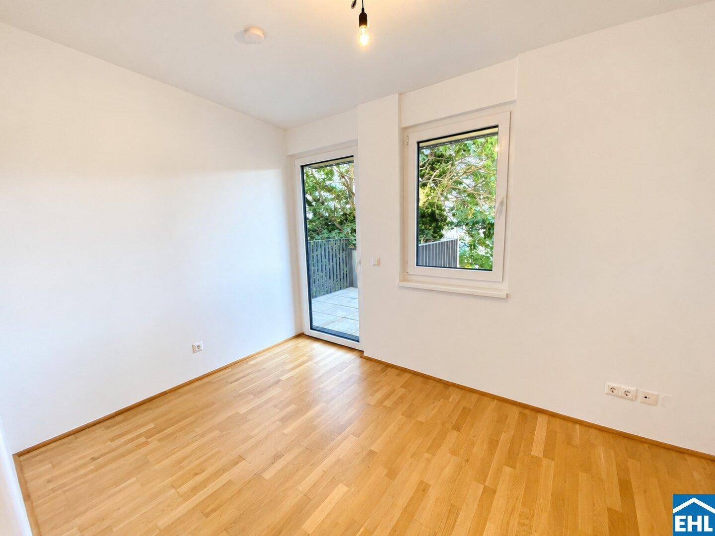 Freundliches Zimmer mit Holzboden, großen Fenstern und direktem Zugang zu einem privaten Außenbereich.
