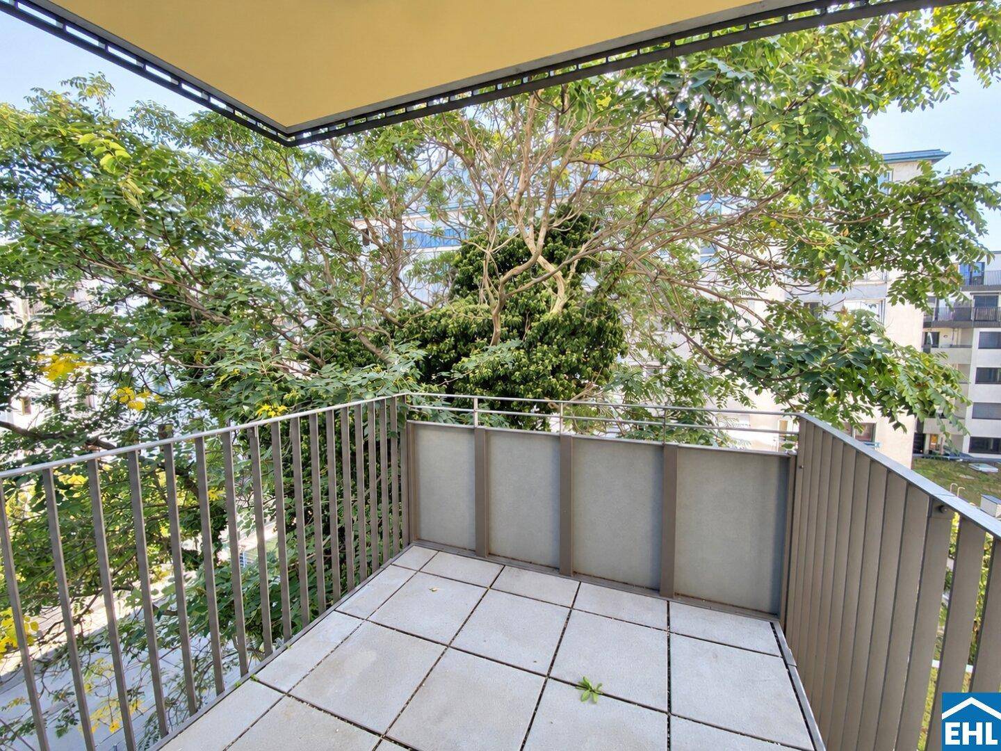Geräumiger Balkon mit Fliesenboden, Metallgeländer und Blick auf einen großen Baum und die Umgebung.