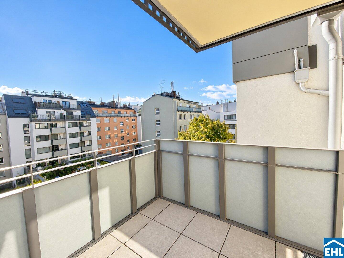 Moderner Balkon mit Fliesenboden und Blick auf die umliegenden Gebäude und den blauen Himmel.