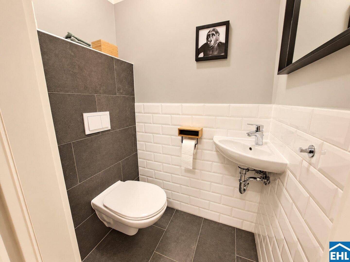 Modernes Gäste-WC mit Wand-WC, kleinem Waschbecken und dunklen Fliesen.
