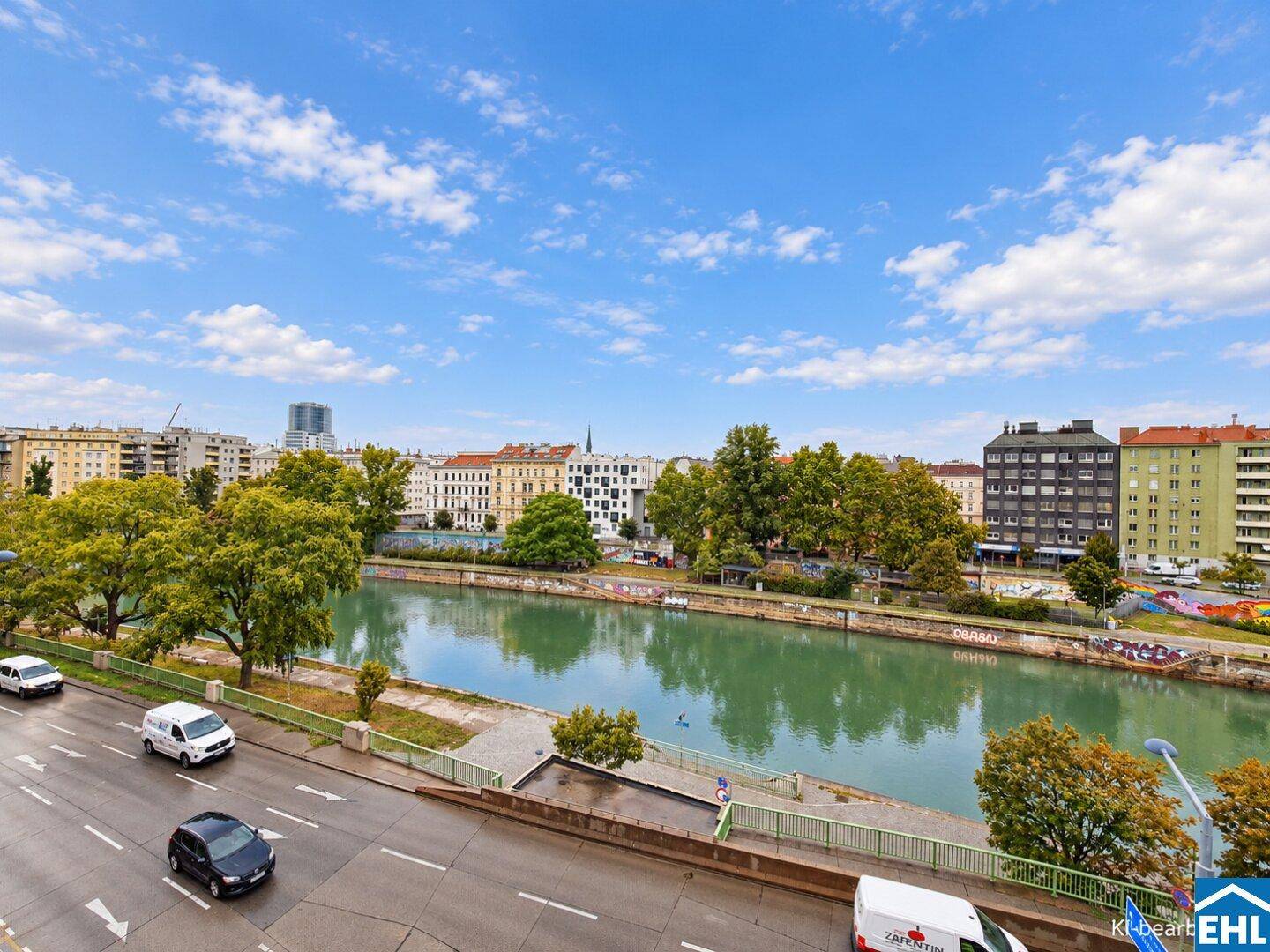 Panoramablick auf den Fluss und die Stadt mit Gebäuden und Bäumen unter blauem Himmel.