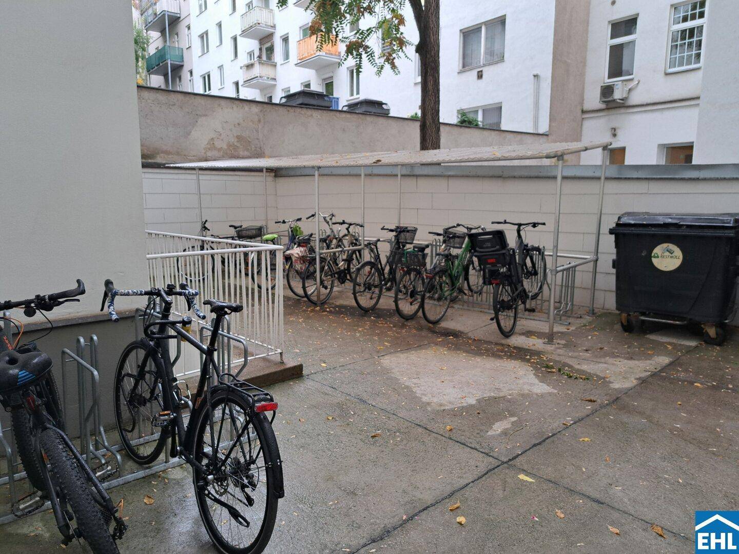 Überdachter Fahrradabstellplatz im Innenhof des Gebäudes mit Mülltonnen.