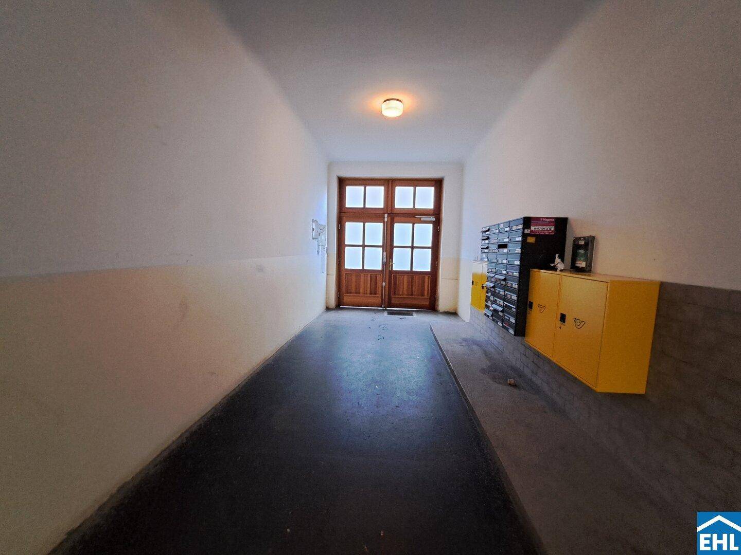 Langer, schmaler Flur im Eingangsbereich des Gebäudes mit Holztüren am Ende.