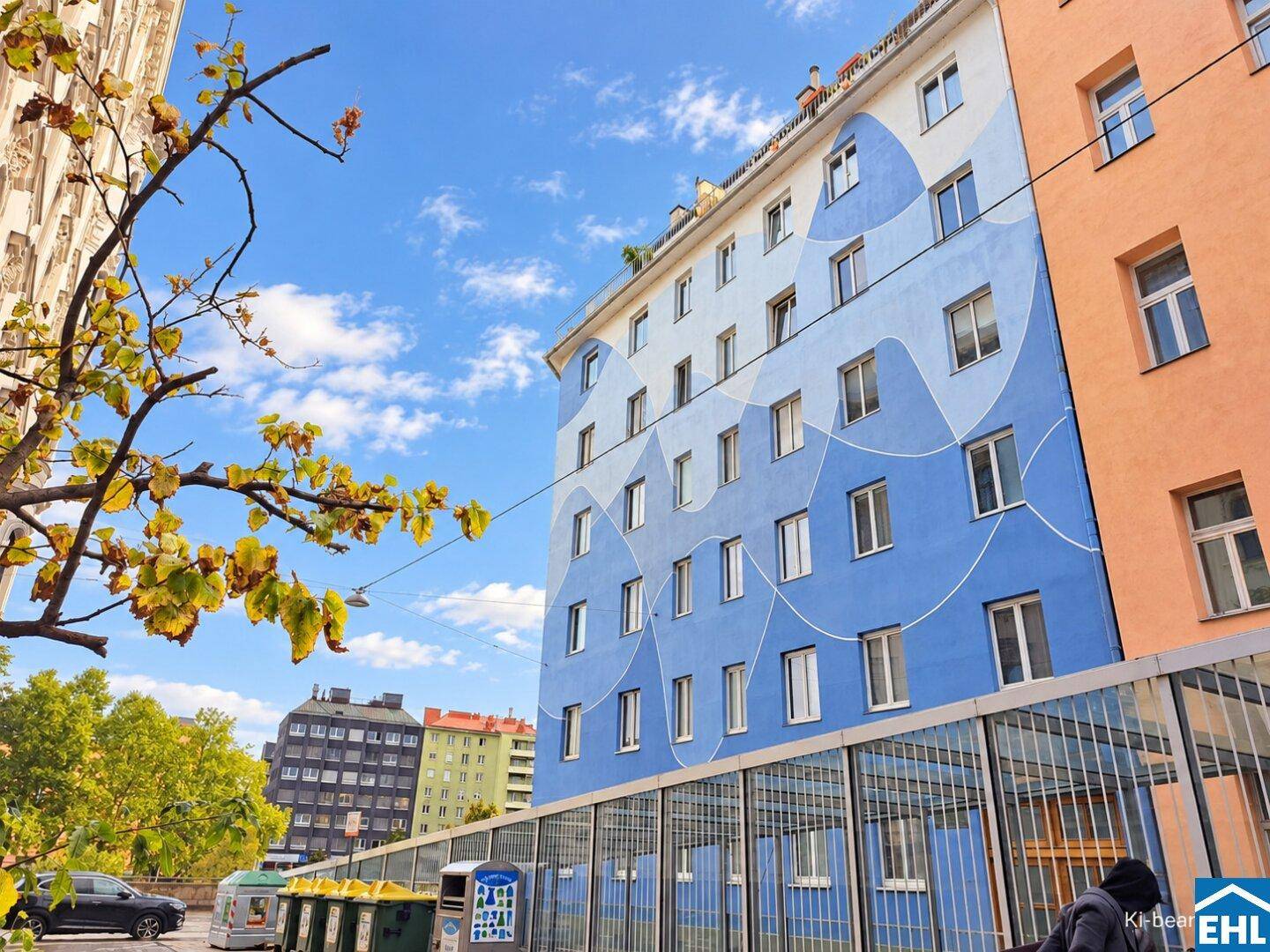Bunte Gebäudefassade mit blauen und weißen Mustern, umgeben von Bäumen und Autos.