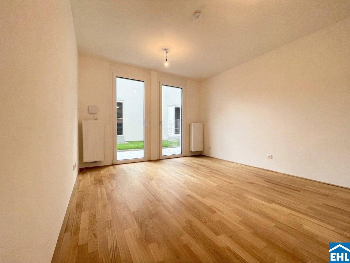 Heller, leerer Raum mit Holzboden, großen Fenstertüren und direktem Zugang zum Garten.