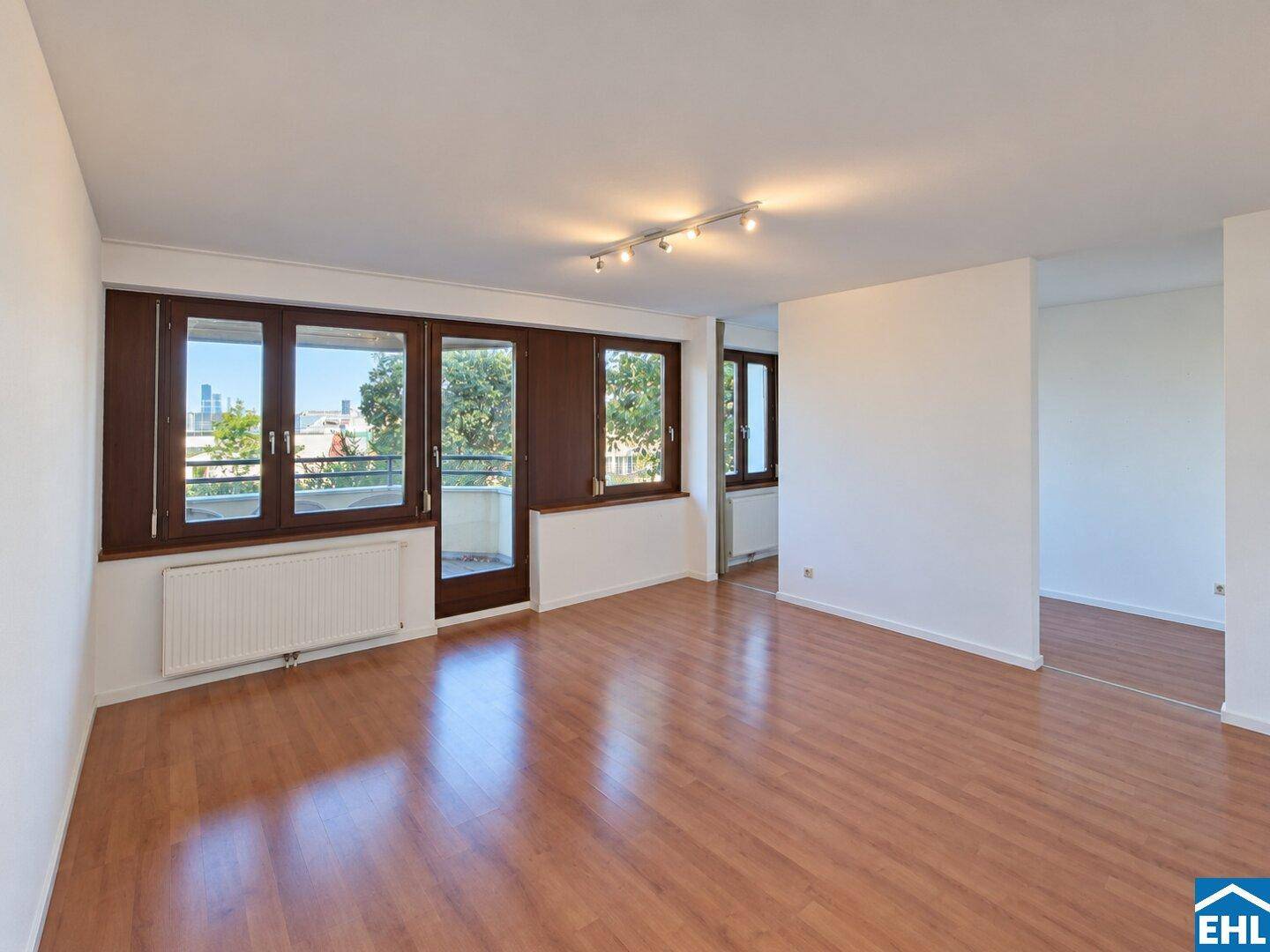 Geräumiger Wohnbereich mit großen Fenstern und Zugang zum Balkon, bietet viel natürliches Licht.