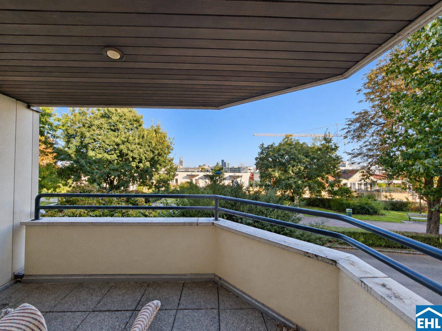 Sonniger Balkon mit weitem Blick über grüne Bäume und die Stadt in der Ferne.