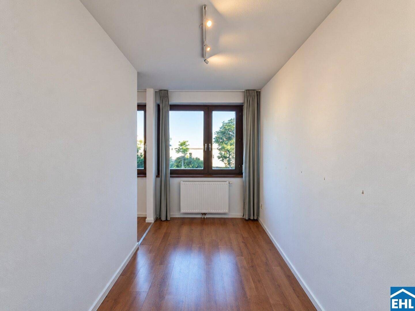 Schmaler Raum mit Fenster und Holzfußboden, vielseitig nutzbar als Büro oder Flur.