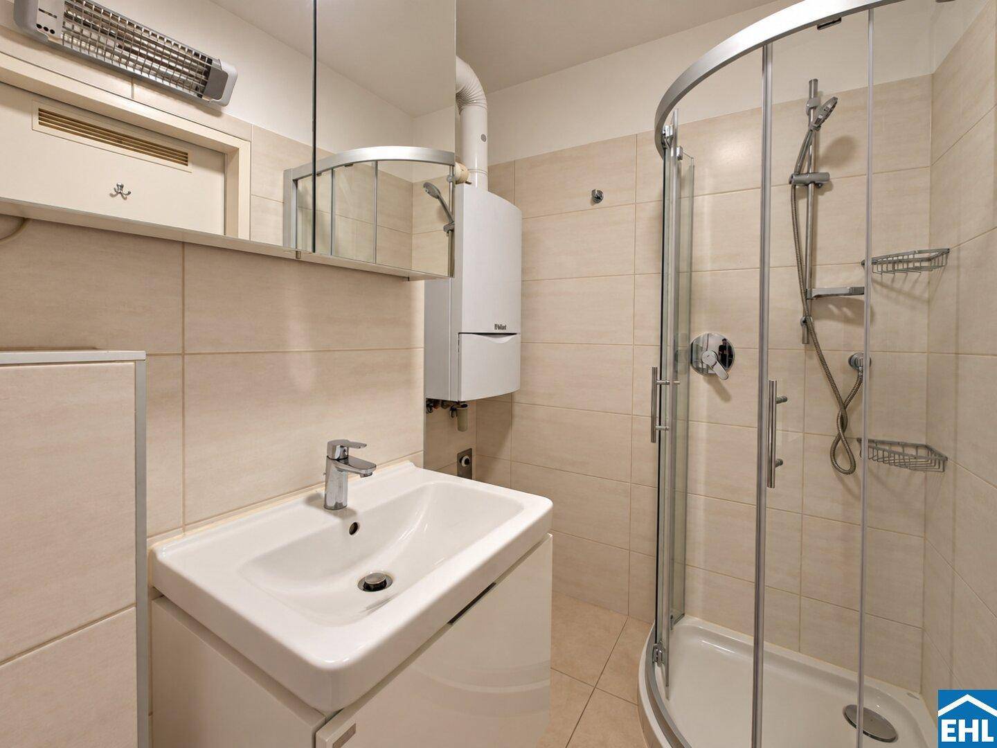Helles Badezimmer mit geräumiger Duschkabine und modernem Waschbecken, sauber gefliest.
