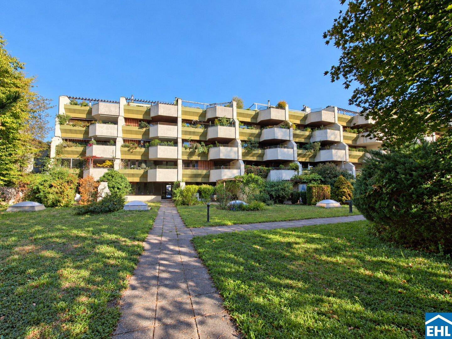 Mehrstöckiges Apartmentgebäude mit zahlreichen Balkonen und gepflegter Grünanlage davor.