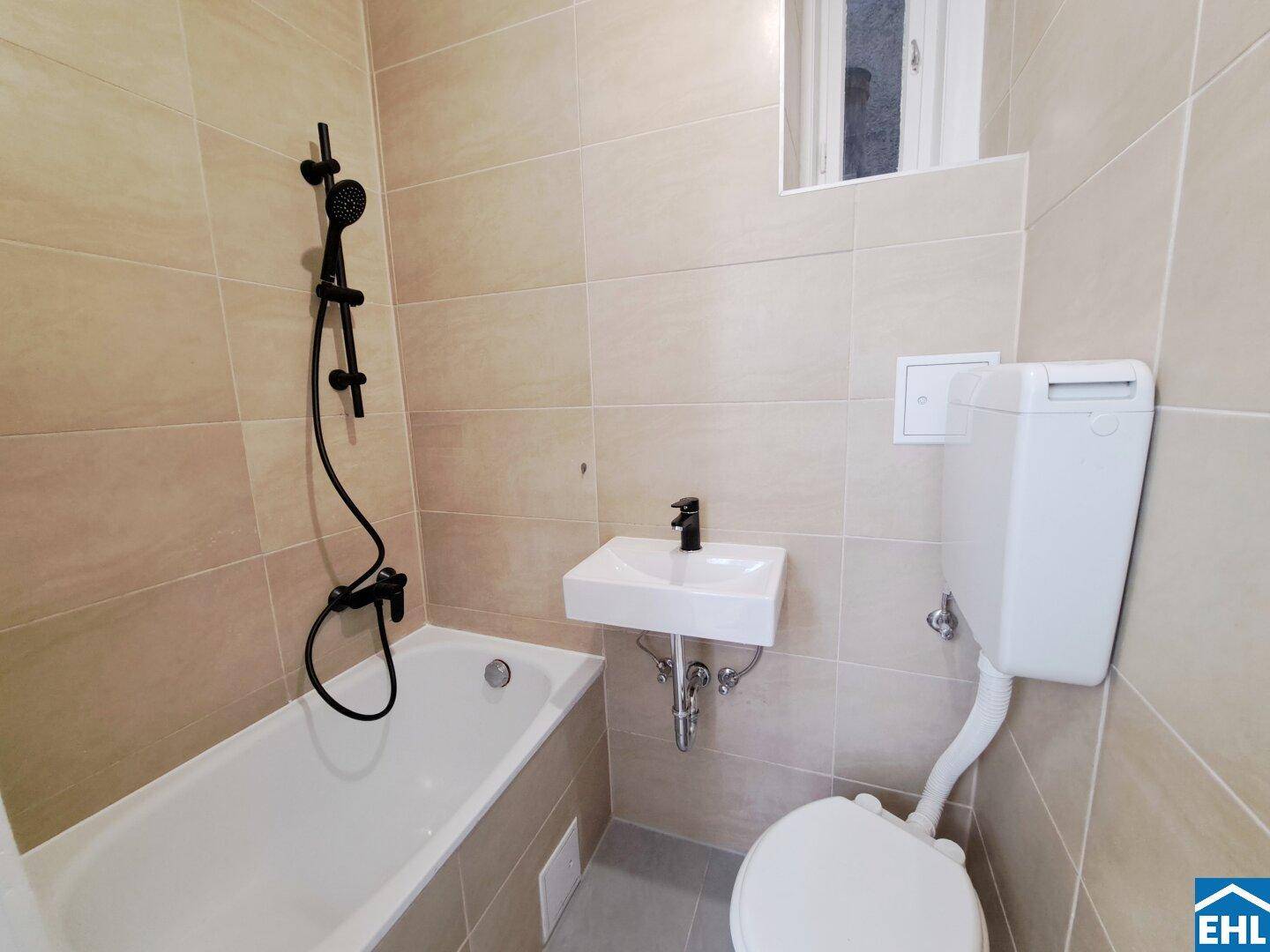 Modernes Badezimmer mit beigefarbenen Fliesen, Badewanne mit Duschfunktion und schwarzen Armaturen.