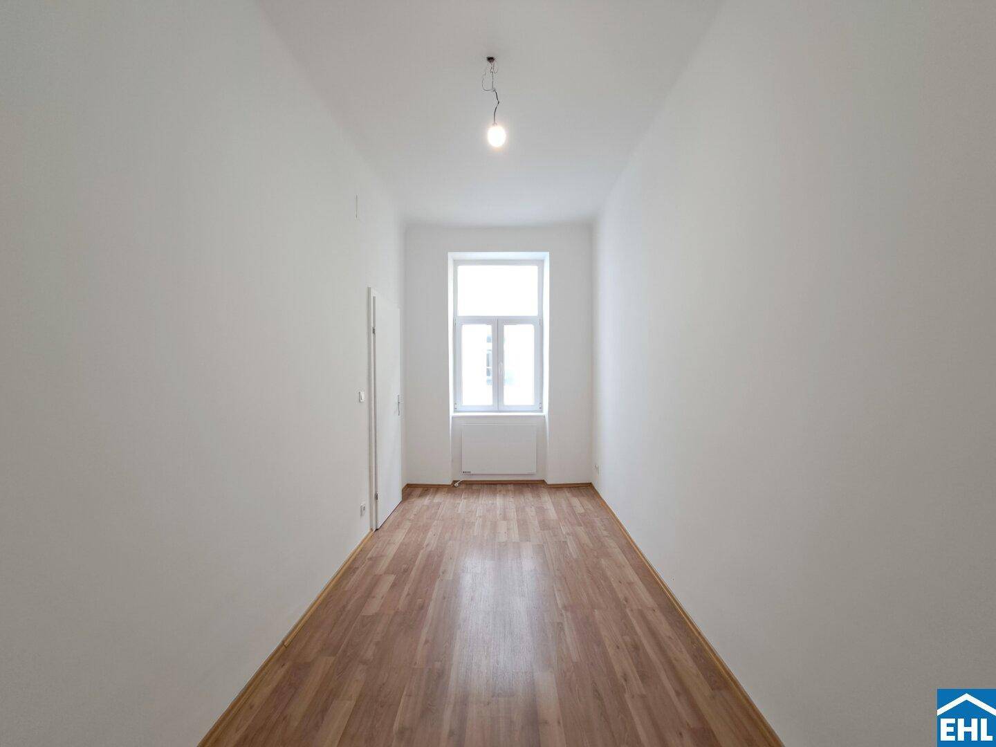 Langer, schmaler Raum mit Laminatboden und einem Fenster am Ende, bietet vielseitige Nutzungsmöglichkeiten.