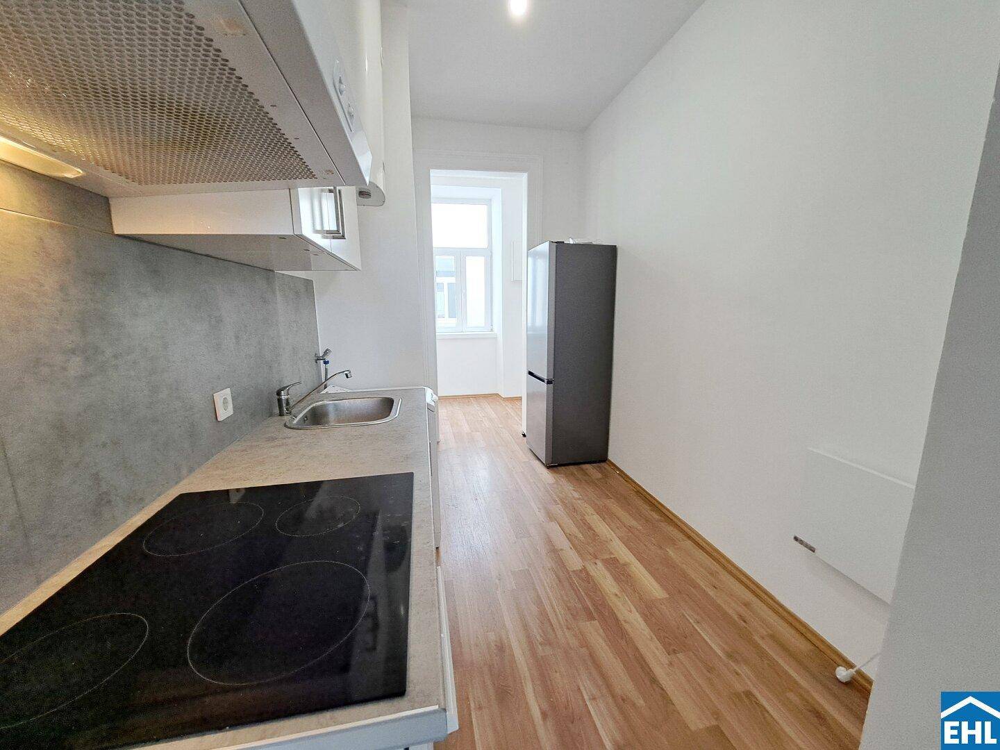 Funktionale Küchenzeile mit Kochfeld, Spüle und Kühlschrank, ergänzt durch ein Fenster für Tageslicht.