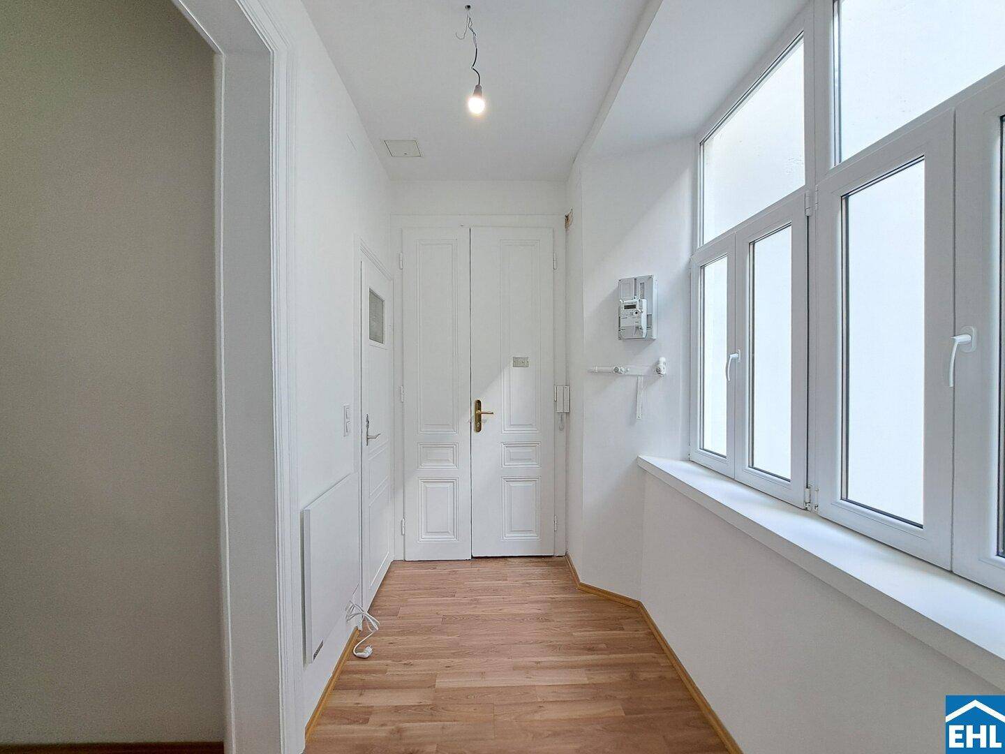 Heller Eingangsbereich mit Laminatboden, großen Fenstern und klassischen Doppeltüren, einladend gestaltet.