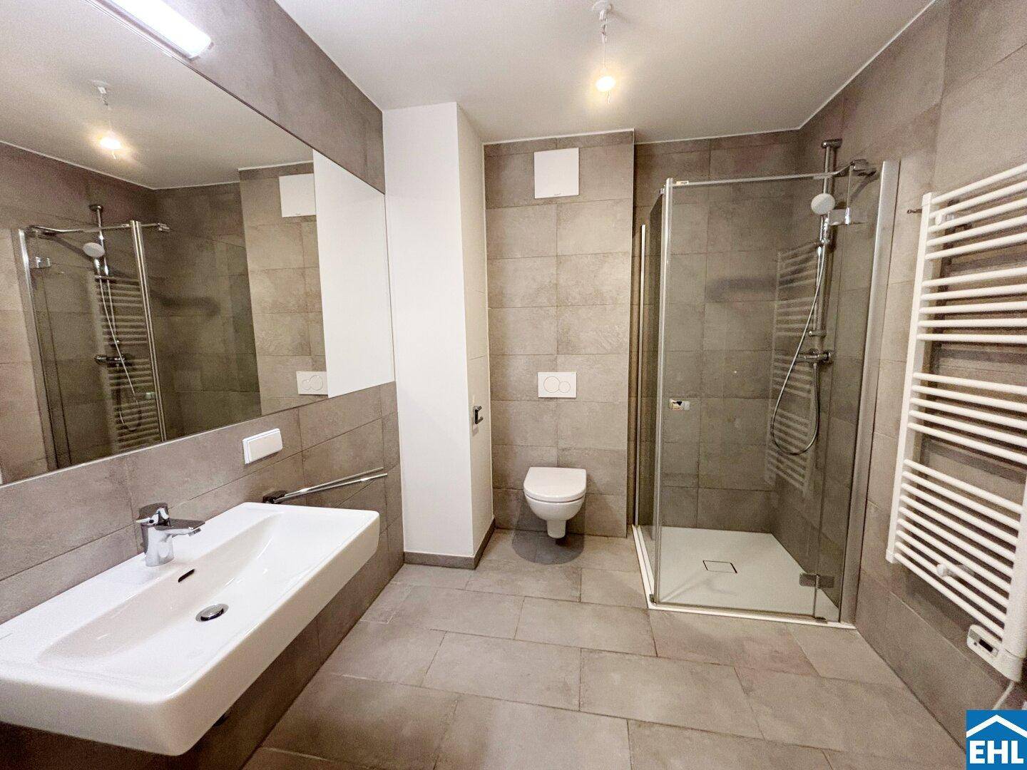 Modernes Badezimmer mit grauen Fliesen, ebenerdiger Dusche, Einzelwaschbecken und beheiztem Handtuchhalter.