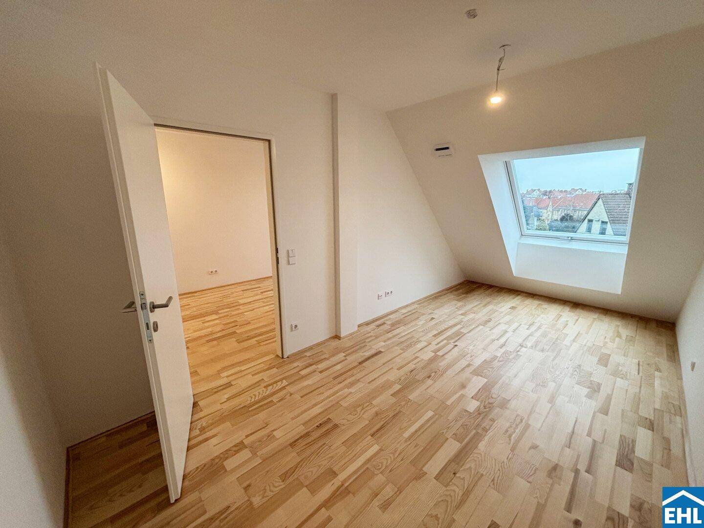 Helles Schlafzimmer im Dachgeschoss mit Holzboden und einem großen Dachfenster, das viel Licht hereinlässt.