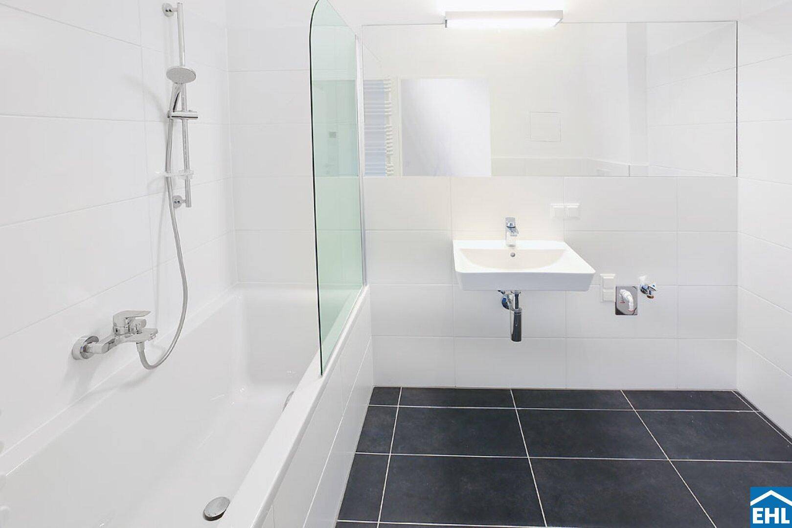 Modernes Badezimmer mit Badewanne, Duschfunktion, Waschbecken und dunklen Bodenfliesen.