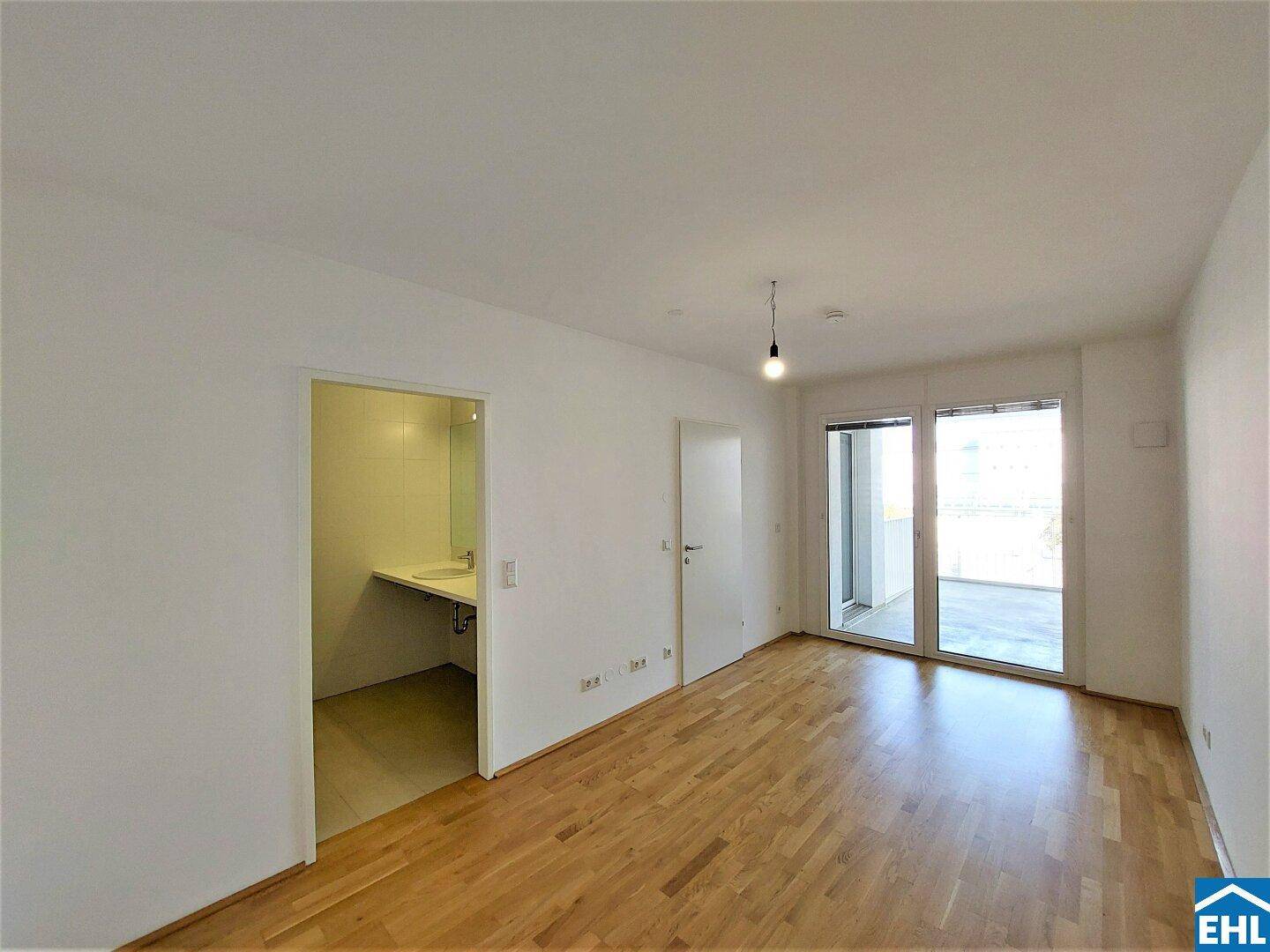 Heller Wohnbereich mit Zugang zu einem kleinen Bad und dem Balkon.