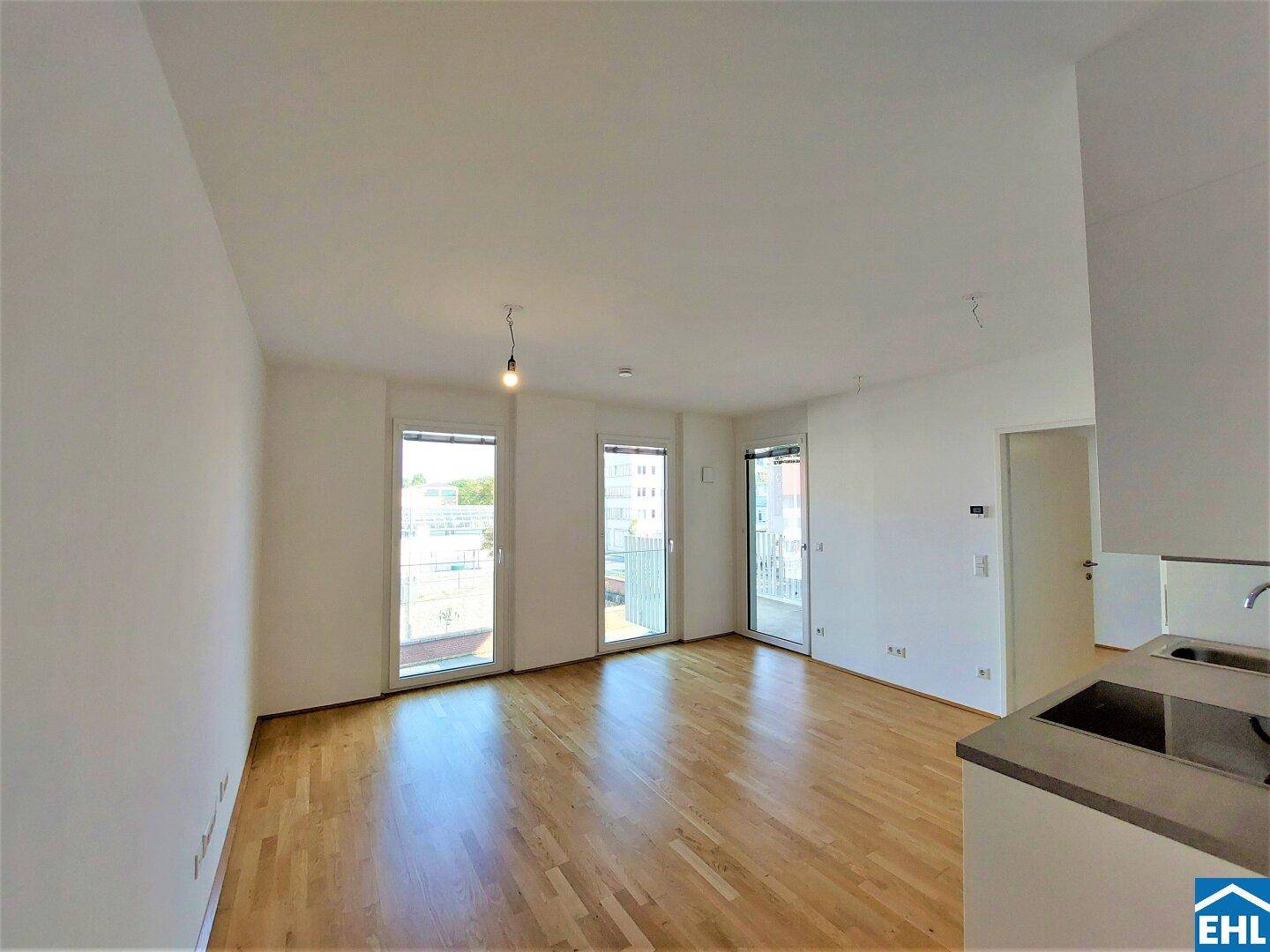 Geräumiger Wohnbereich mit großen Fenstern, die viel Tageslicht hereinlassen und Parkettboden.