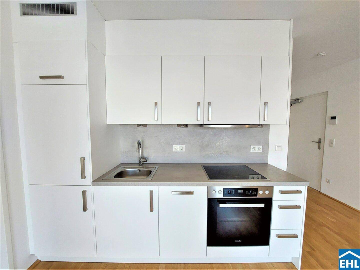 Moderne Küchenzeile mit weißen Schränken, integriertem Backofen und Induktionskochfeld.