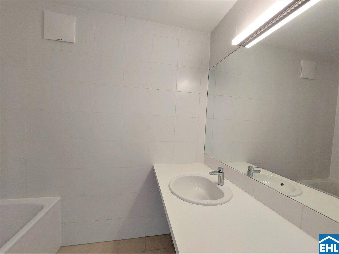 Modernes Badezimmer mit weißen Fliesen, Waschbecken, großem Spiegel und Badewanne.
