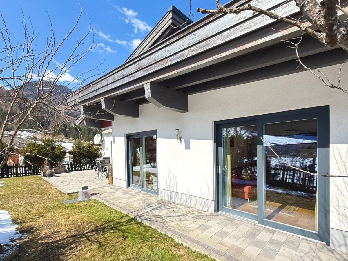 Seitliche Terrasse mit gepflastertem Bereich und Zugang zum Garten, umgeben von Natur.