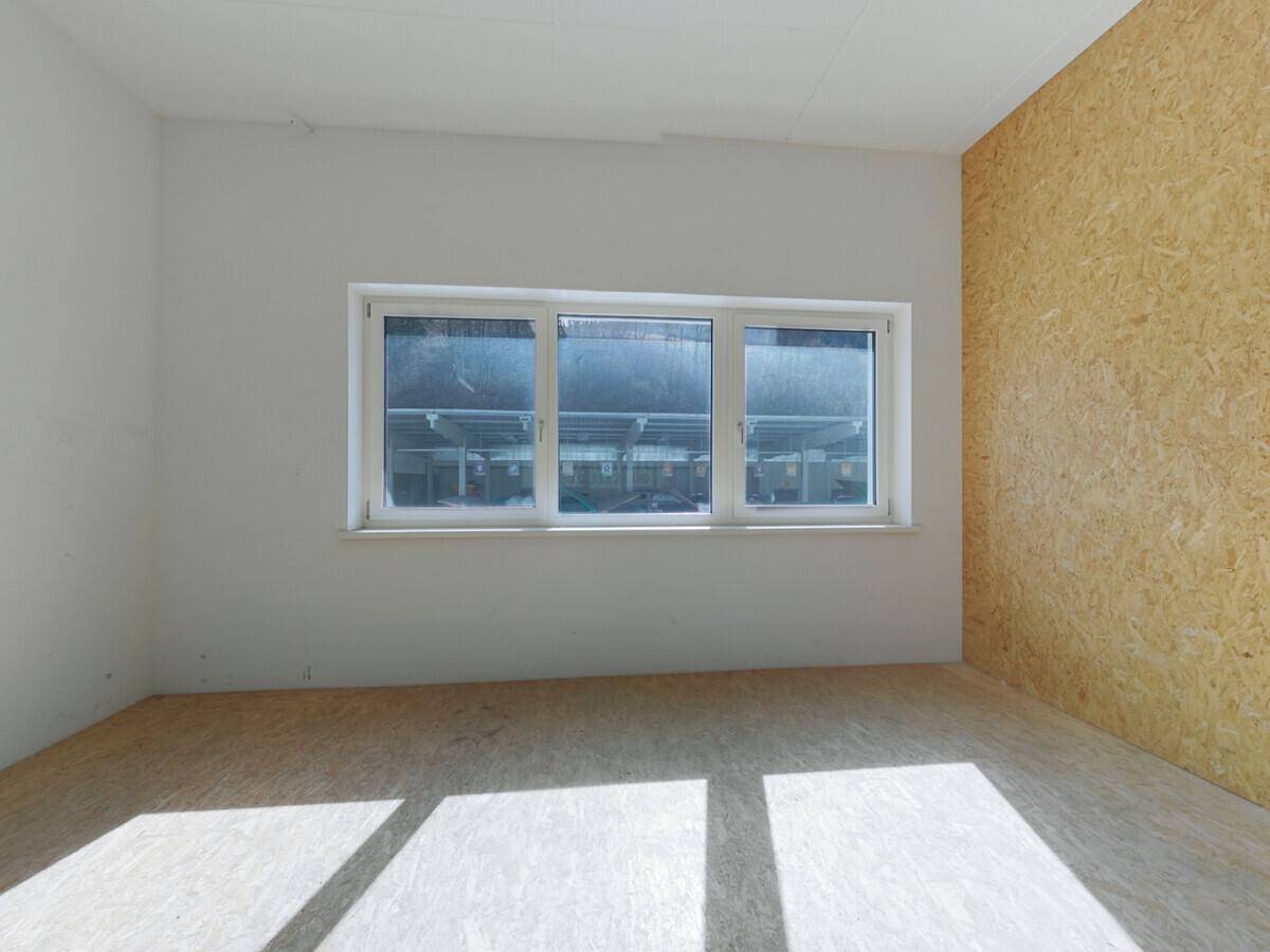 Heller, leerer Raum mit OSB-Boden, weißen Wänden und einem großen Fenster, das viel natürliches Licht hereinlässt.