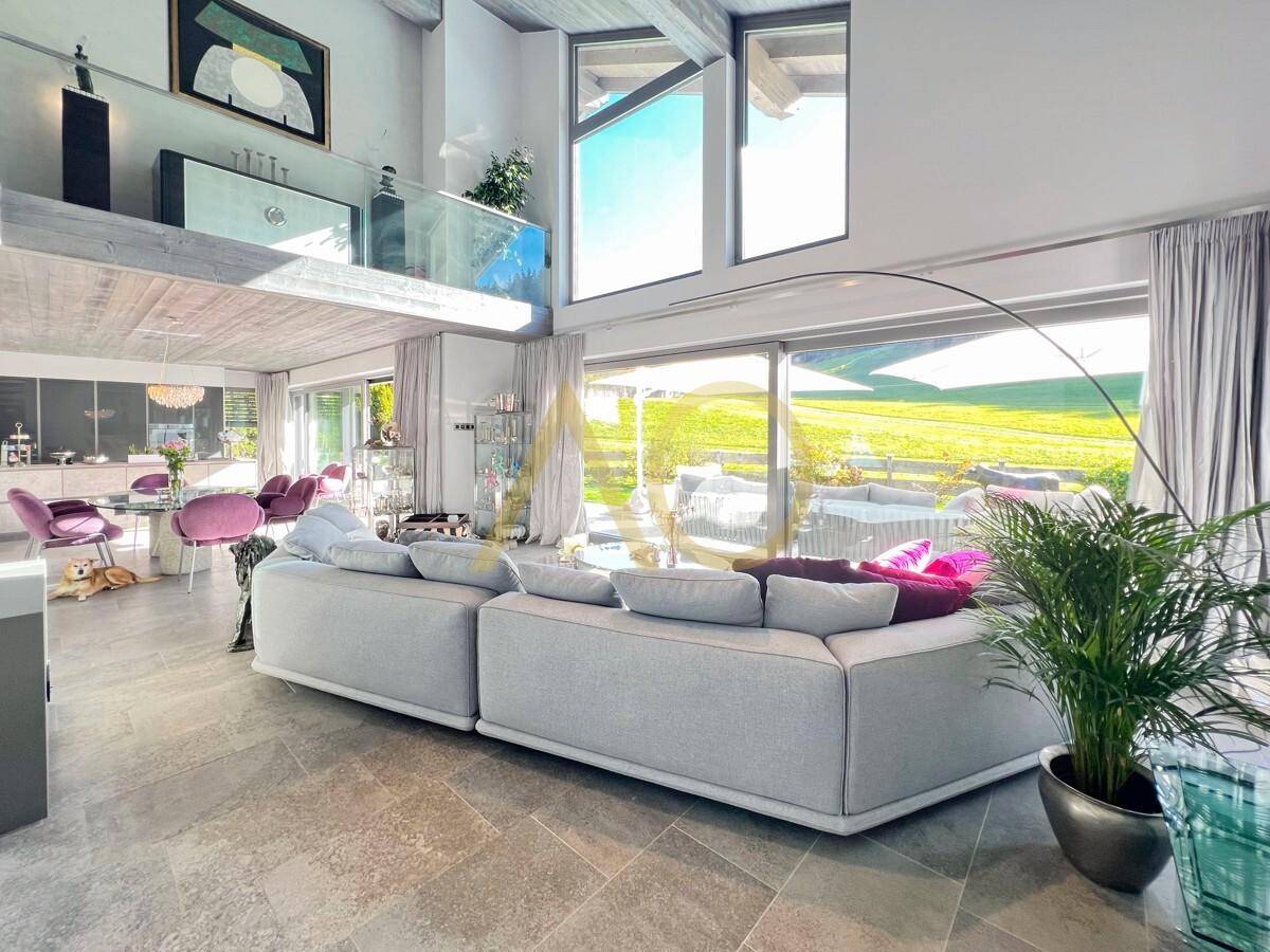 Großzügiges Wohnzimmer mit hohen Decken, bequemer Couch und weitem Blick ins Grüne.