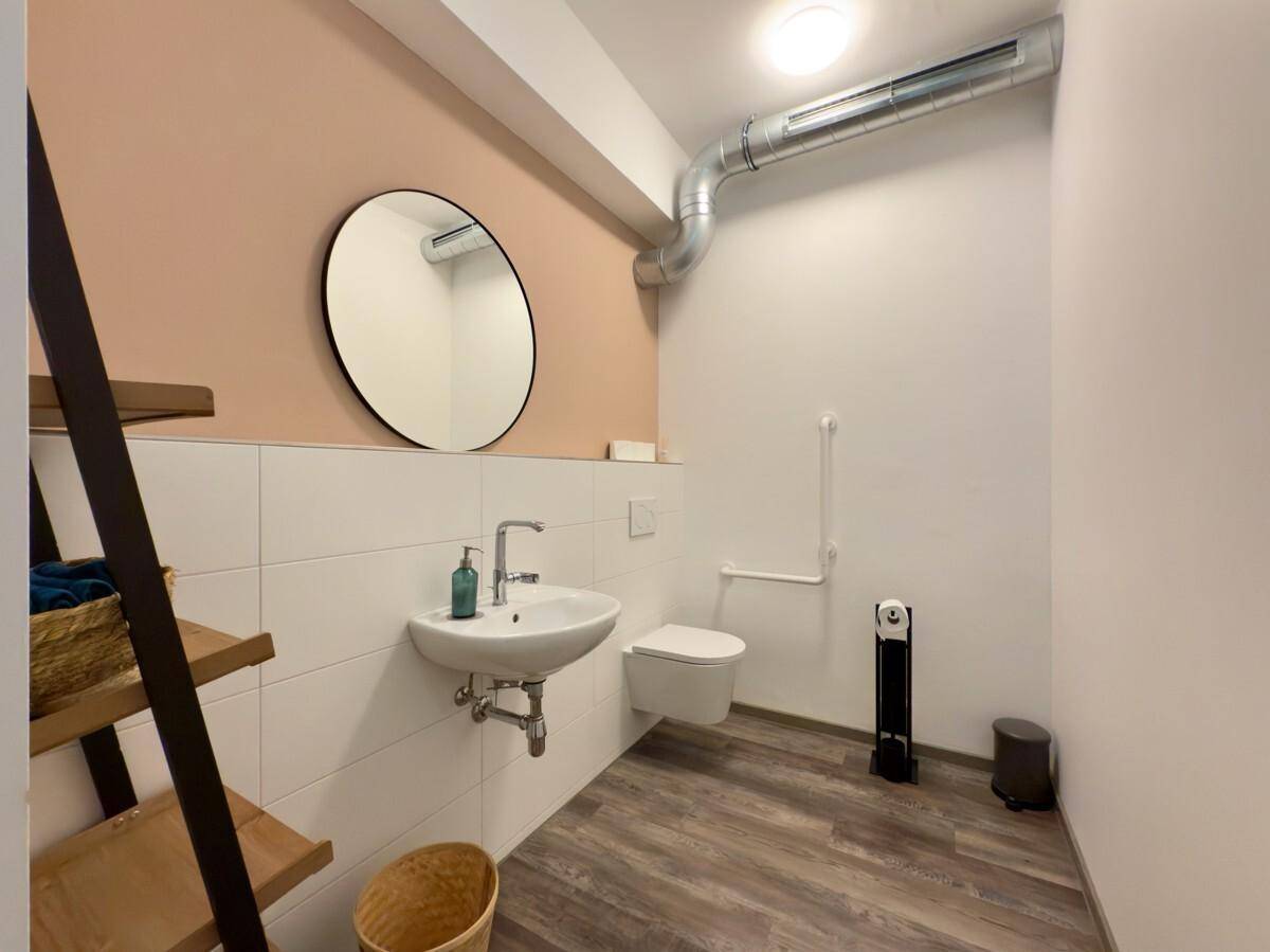 Modernes WC mit Waschbecken, Spiegel und Haltegriffen für Barrierefreiheit.