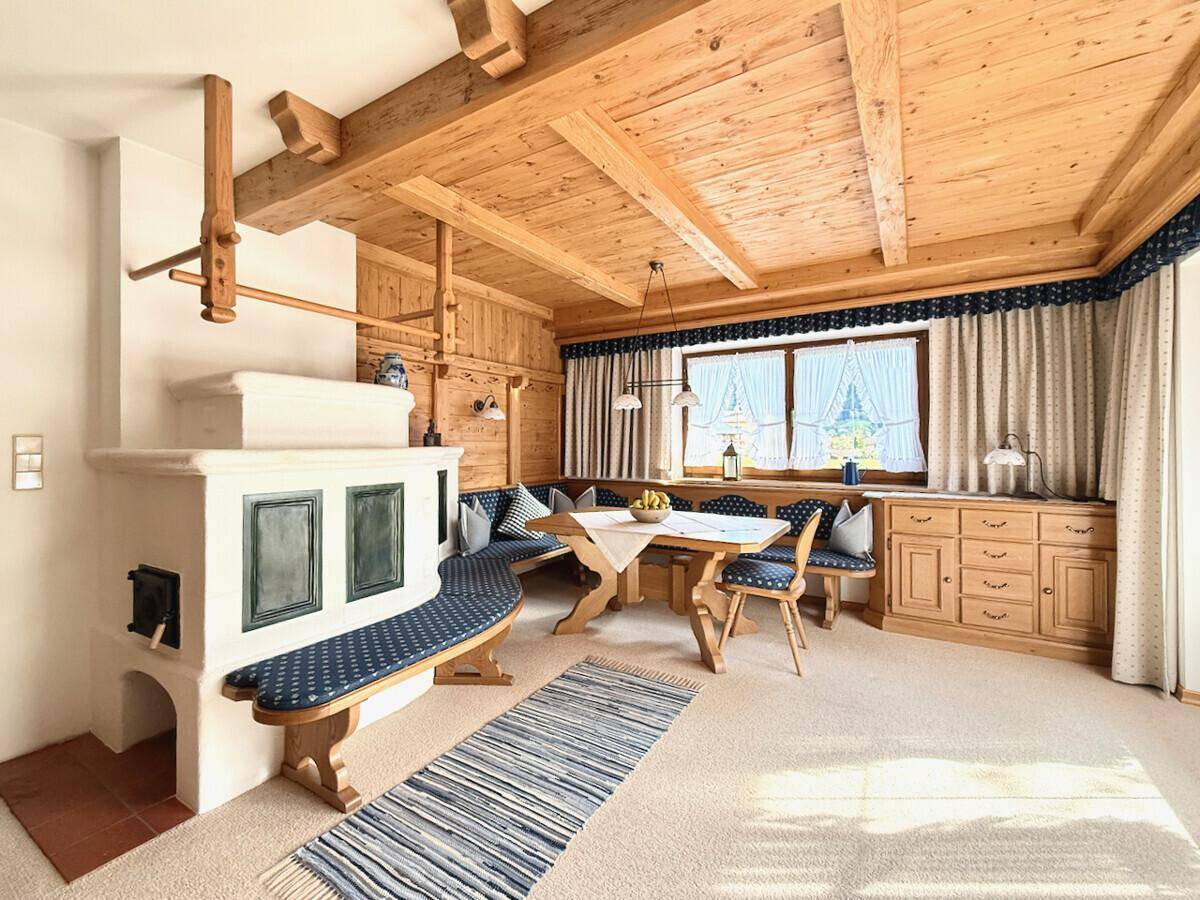 Heller Wohn-Essbereich mit Kachelofen, Holzbalkendecke und Zugang zur Terrasse.