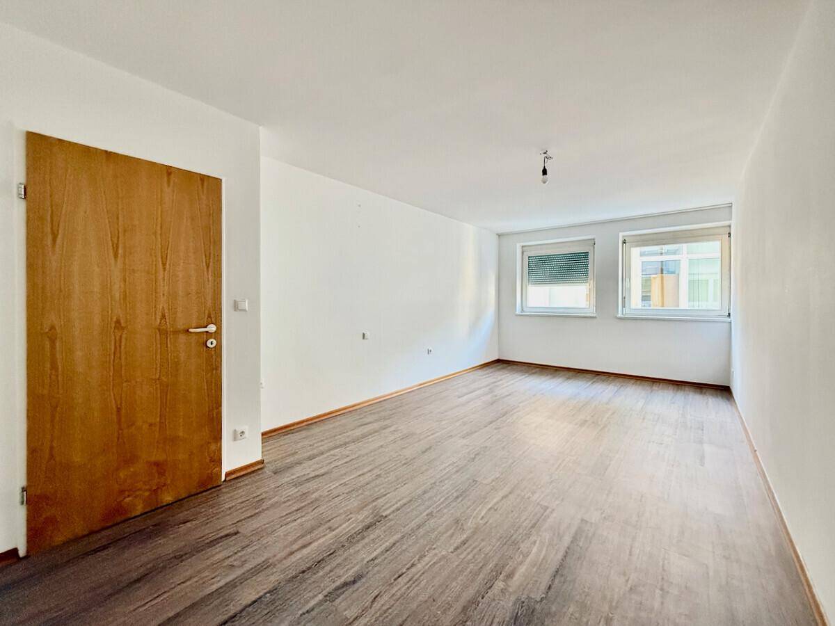 Helles Zimmer mit Laminatboden, weißen Wänden und einer Holztür.