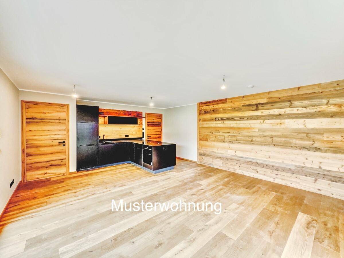 Offener Wohnbereich einer Musterwohnung mit Holzboden, Holzwand und moderner dunkler Küche.