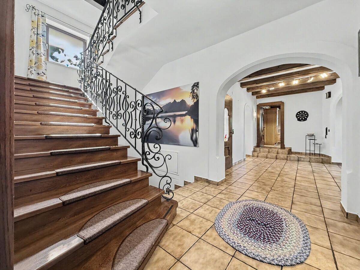 Elegante Holztreppe mit schmiedeeisernem Geländer in einem gefliesten Eingangsbereich.