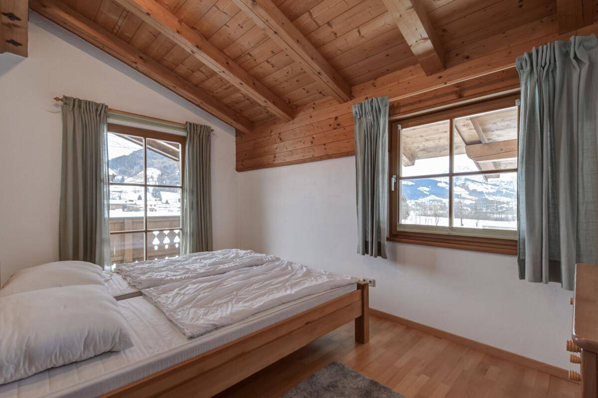 Gemütliches Schlafzimmer mit Holzbalkendecke, Parkettboden und Fenstern mit Bergblick.