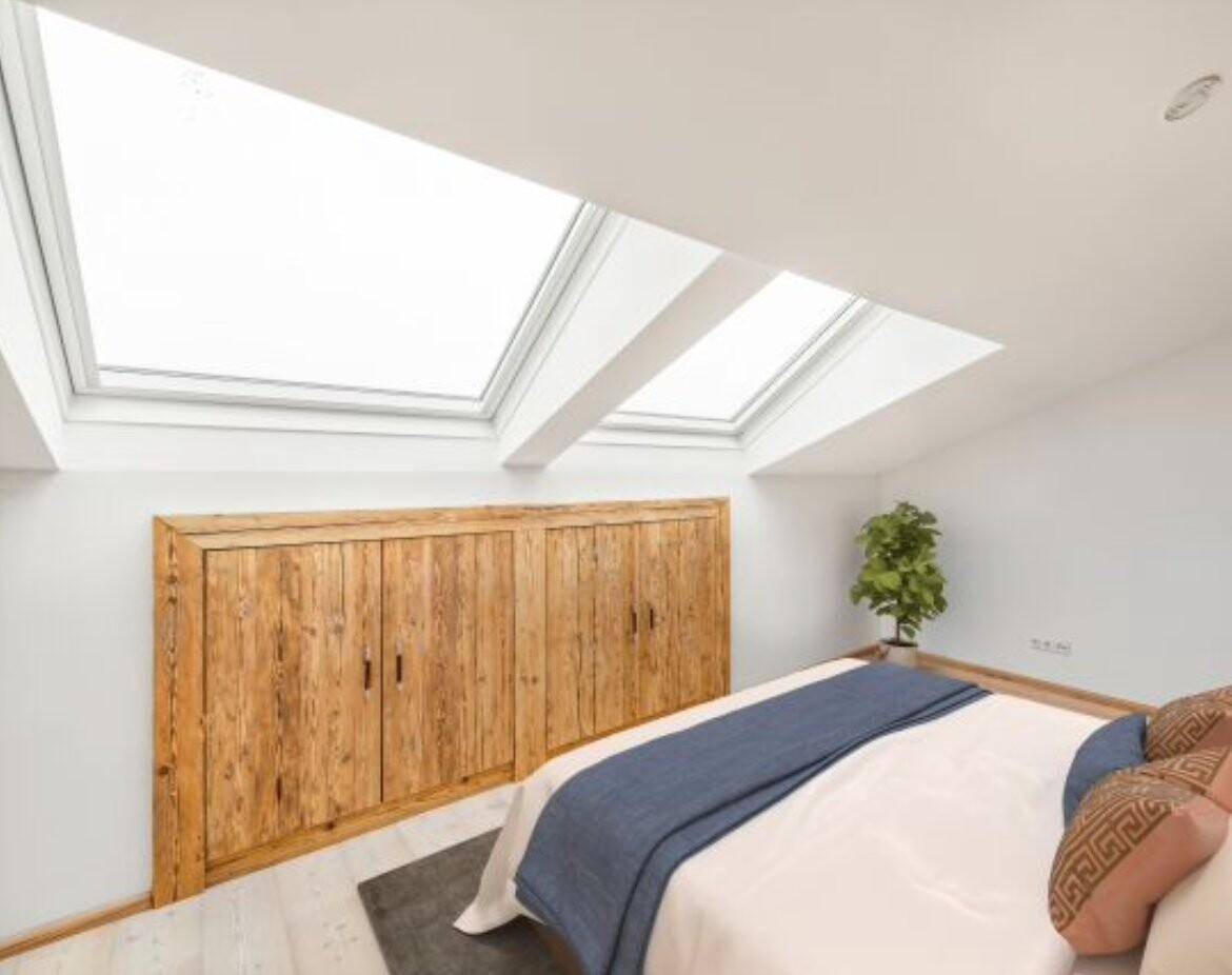Lichtdurchflutetes Schlafzimmer im Dachgeschoss mit zwei großen Dachfenstern und rustikalen Holzschränken.