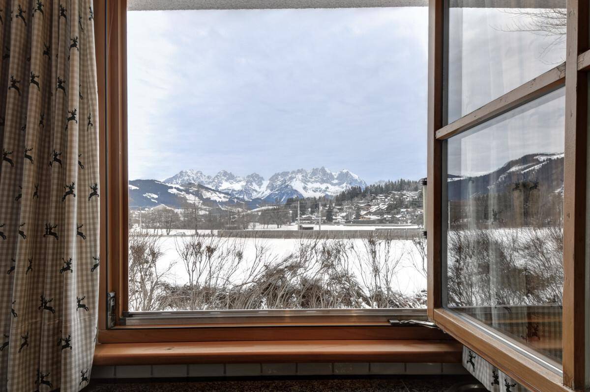 Fensterblick auf die weite, verschneite Landschaft und die beeindruckende Bergkette am Horizont.