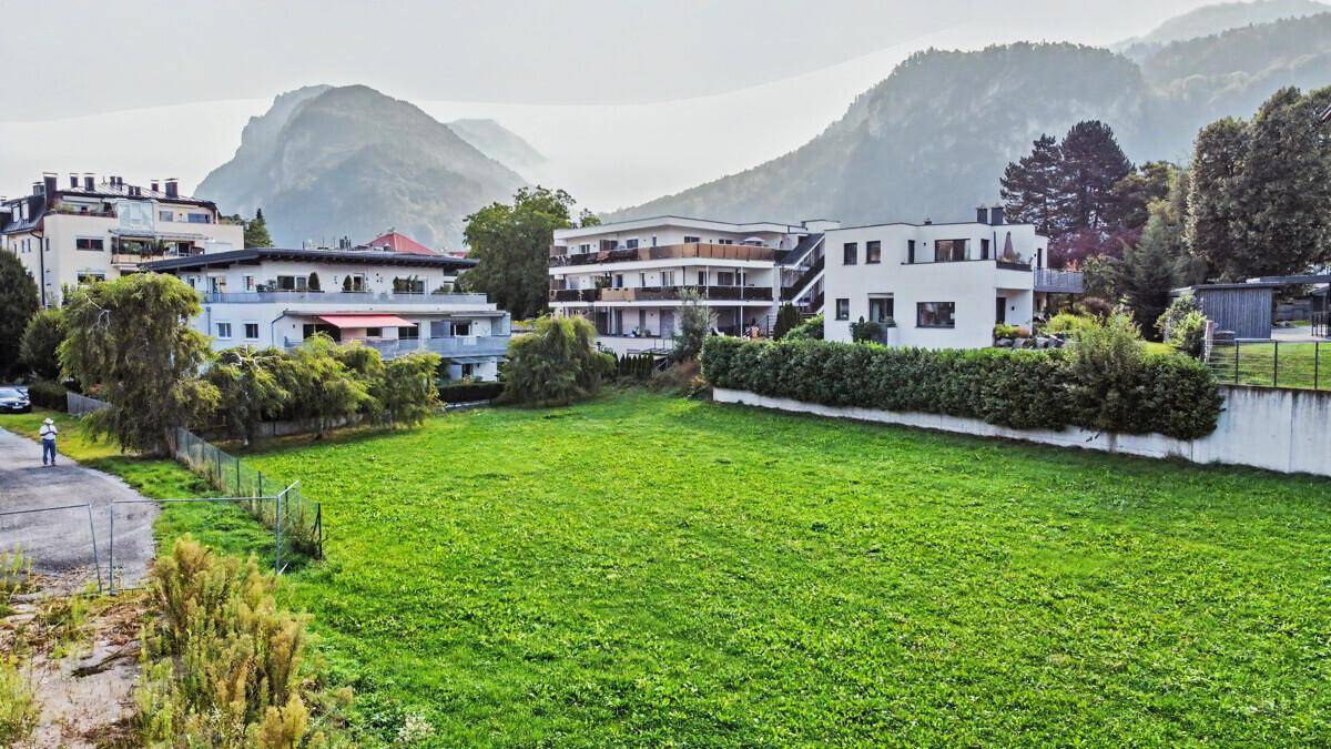 Weitläufige Grünfläche mit umliegenden Gebäuden und nebligen Bergen im Hintergrund.