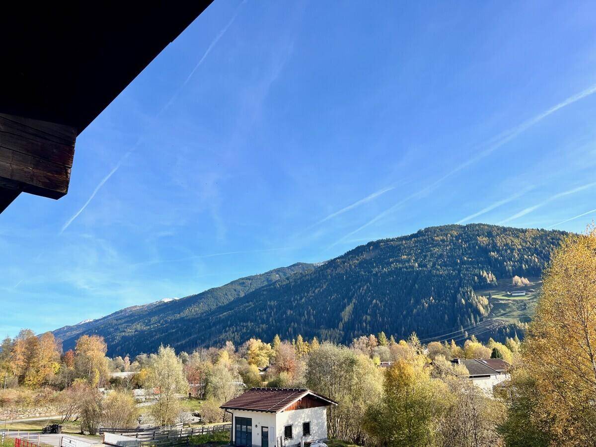 Weitläufiger Blick auf die umliegende Berglandschaft mit herbstlicher Vegetation unter blauem Himmel.