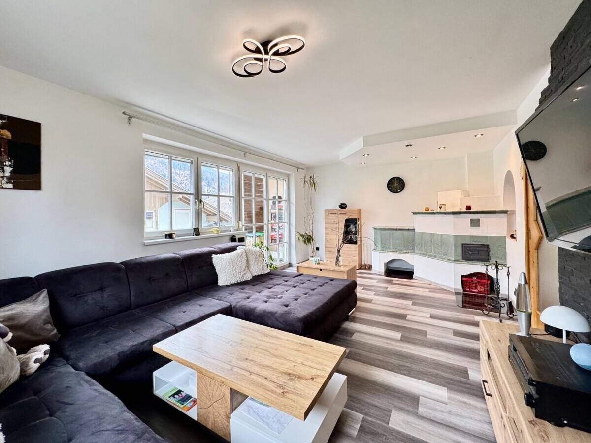 Gemütliches Wohnzimmer mit großem Sofa, modernem Kachelofen und Blick ins Grüne.